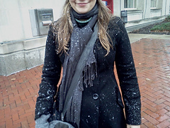 A woman in a black coat with snowflakes falling.